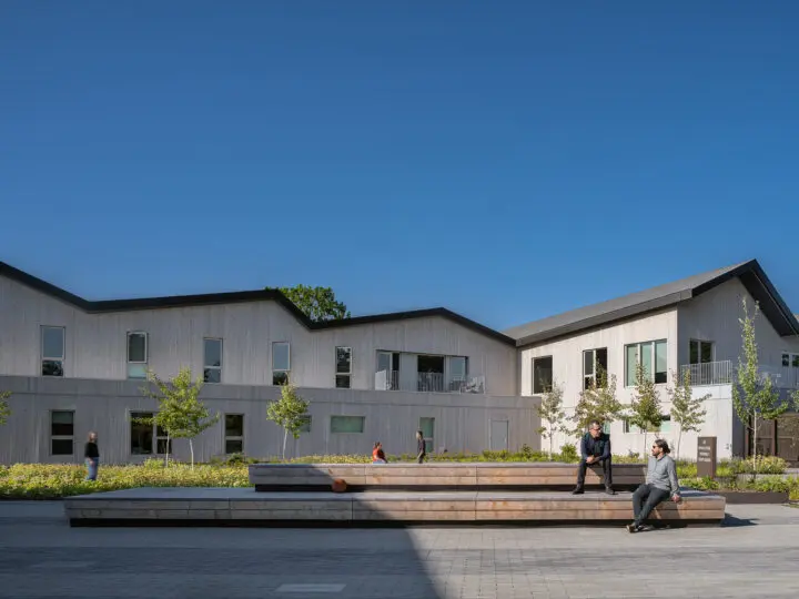 A lengthy bleacher-like wooden bench defines the outer edge of the courtyard's basketball area.
