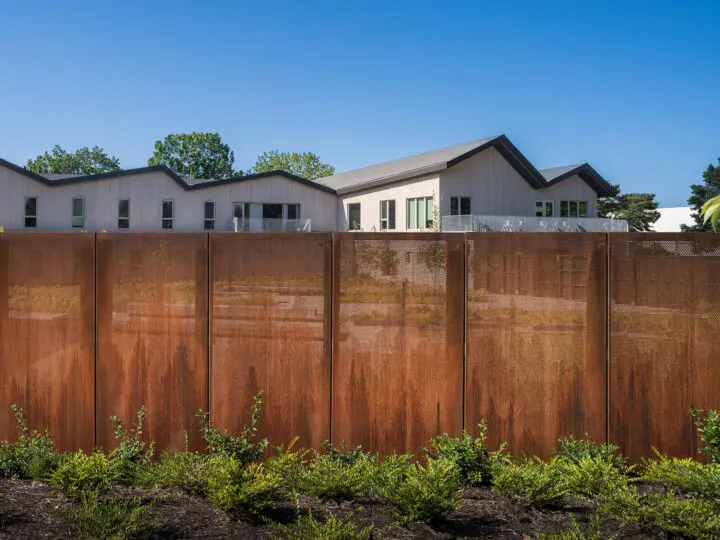 A close-up shows the perforated rusted metal panels that create the fence that encloses the courtyard.