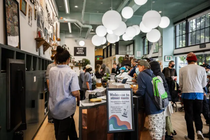 A group of vendors gathers around the tall desk in the resource center, picking up papers to sell.