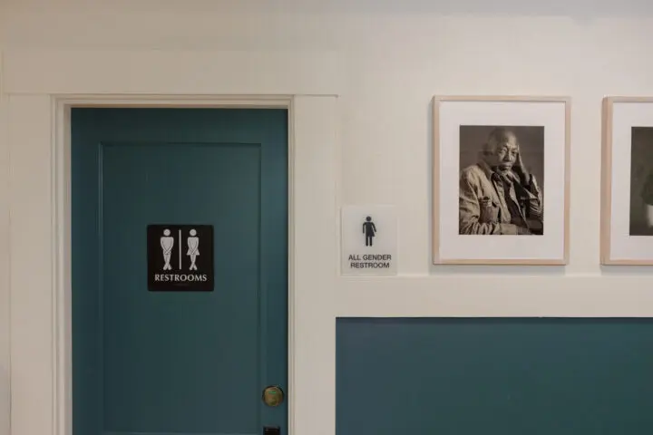 A single-user staff restroom includes inclusive signage posted near a row of framed black-and-white portraits.