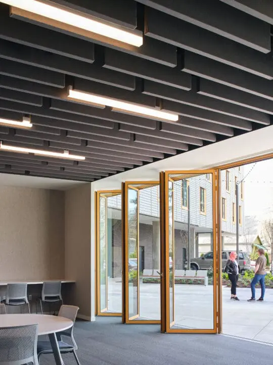 View from inside 72Foster’s ground-floor community room looking out through its open Nana Walls to two people standing outside talking.