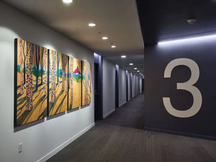 72Foster’s 3rd-floor hallway features warm gray flooring, four vibrant yellow paintings on the wall, and a large “3” painted on the wall.