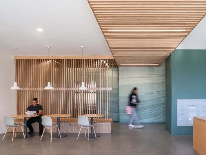 A person sits reading a paper while another person is walking into a hallway at The Aurora.
