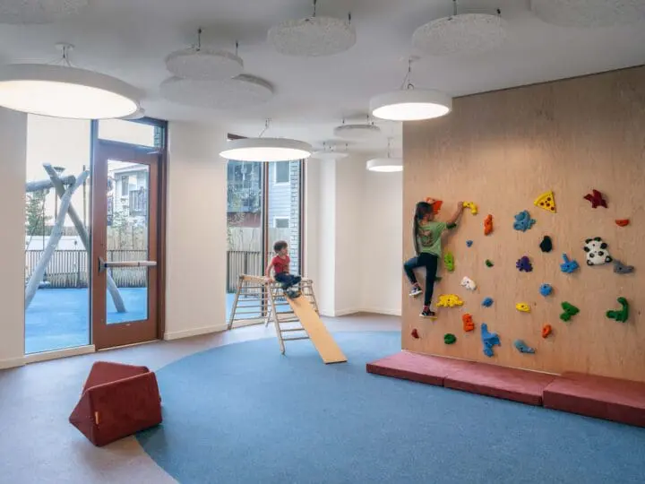 In the indoor/outdoor playroom at The Aurora, one child slides down a slide while another climbs a rock wall.