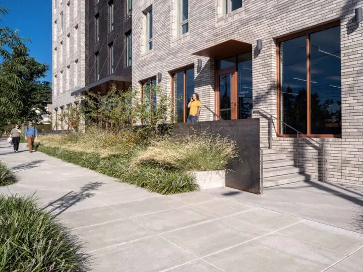 A person in a yellow shirt stands talking on the phone by the front door of the apartment building, The Aurora.