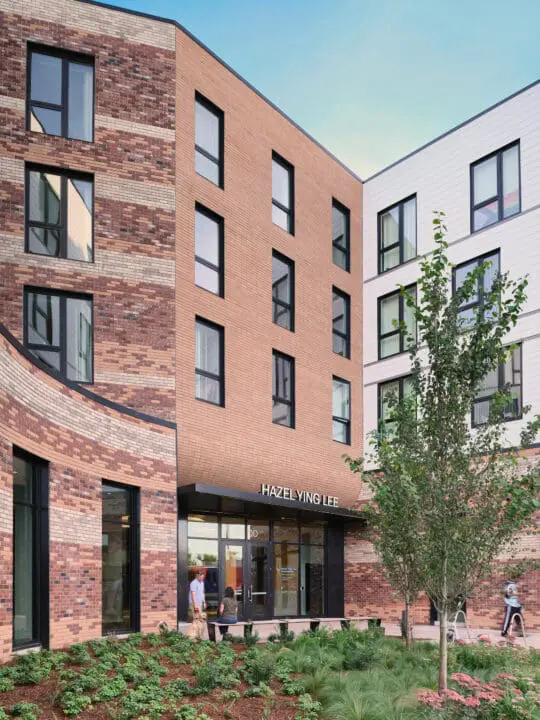 The four-story building mass wraps around the entry courtyard with dynamic angular faces and curved brickwork.