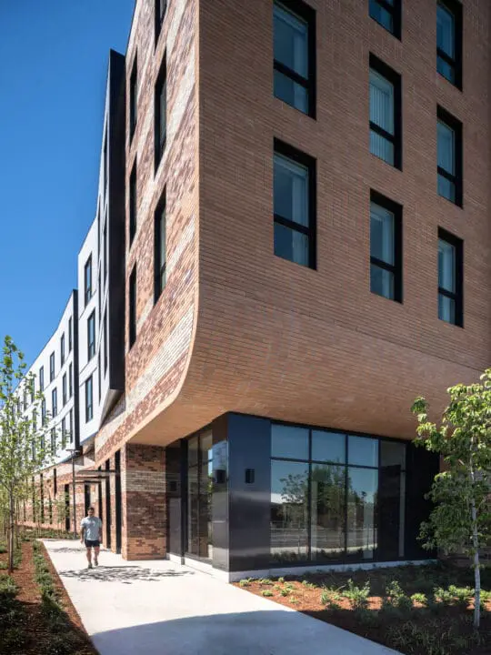 Floor-to-ceiling glass meets a curved brick overhang at the transition between ground and residential floors.