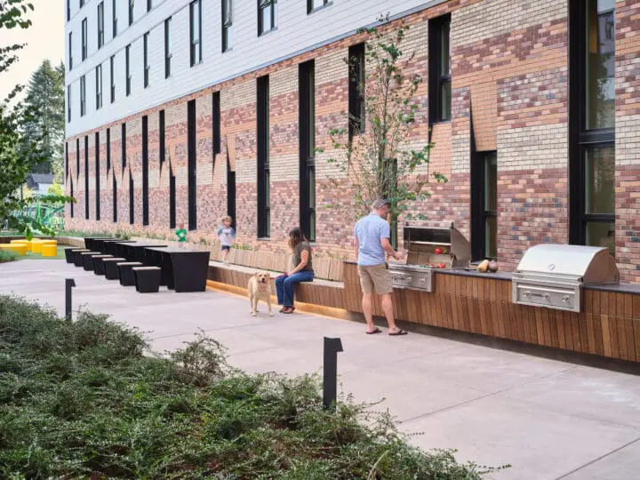 A long wooden bench travels the length of the Southern courtyard along a play area, picnic seating, and ends at an outdoor grill.