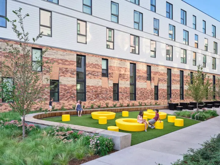 A group of kids is playing on circular yellow seats in a grassy area at the end of the southern courtyard.