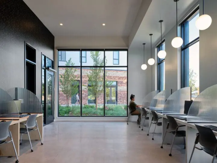 Computer workstations line the sides of an open room, with large windows at the back to look outdoors.