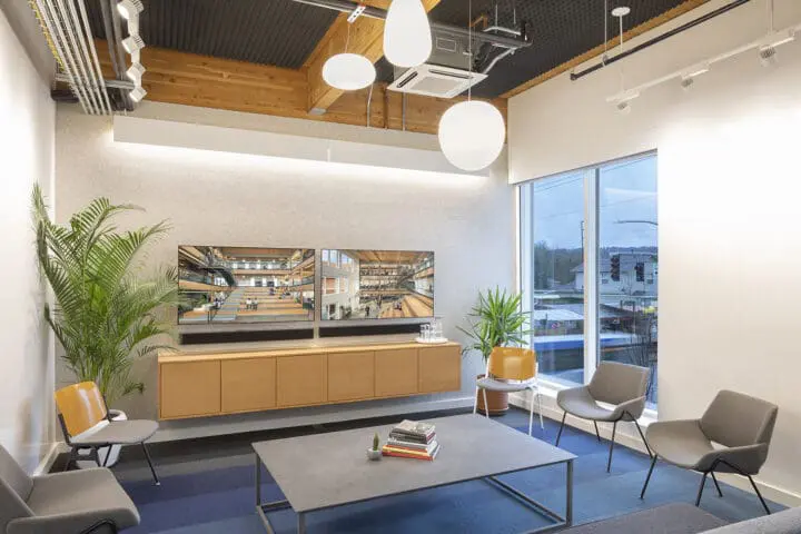 A lounge-like meeting room with a low, grey coffee table and a circle of upholstered chairs over a navy carpet.