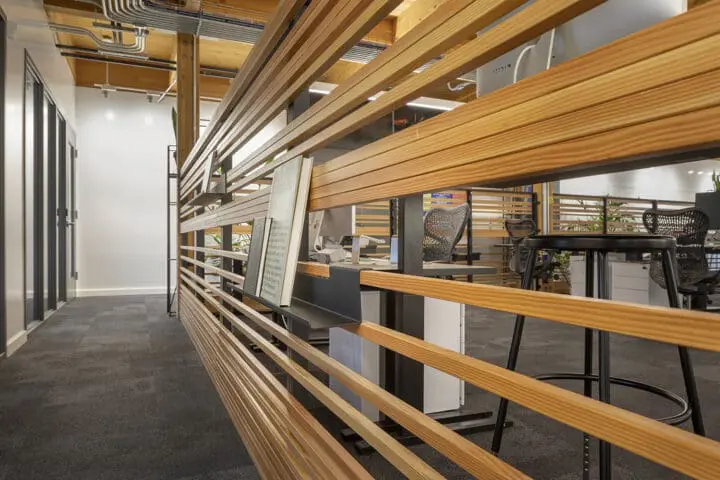 A close-up on an office partition shows folded metal bookshelves hung from honey-colored wood slats.