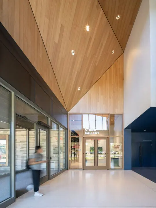 The dramatic interior entrance to the Stirek Gallery features a tall, geometric wood ceiling folding down towards the doors.