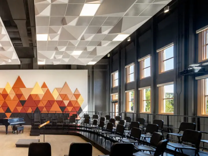 A large classroom rehearsal space features concrete floors and stepped seating with music chairs in a U-shaped configuration.